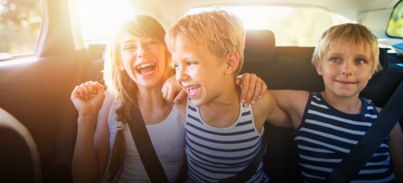 Three smiling kids enjoying their road trip on the backseat of the car